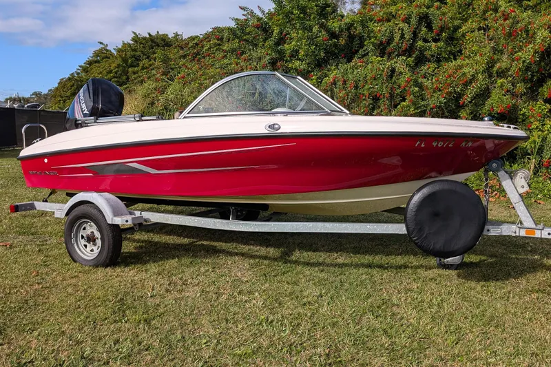 Slide: The Image of 2016 Bayliner 160 Bowrider on trailer, red and white, parked on grass. - 0