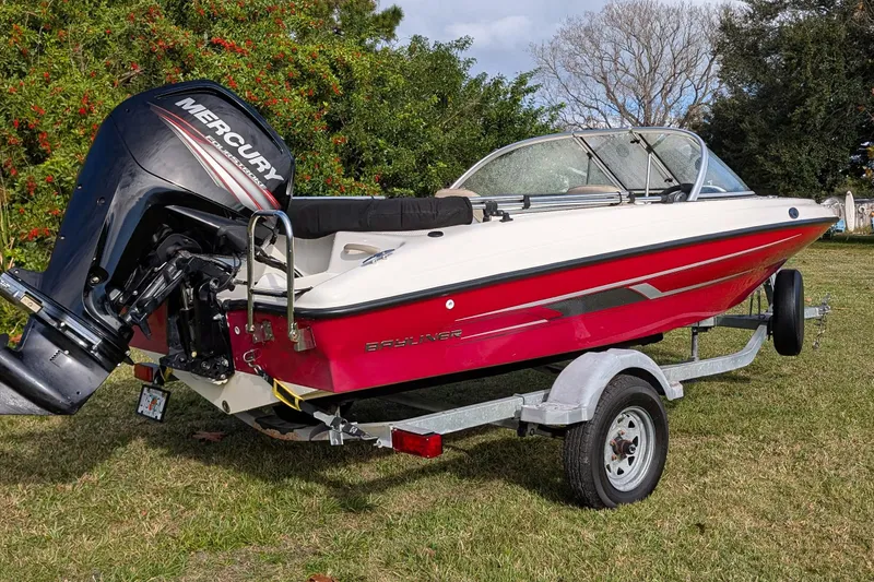 Slide: The Image of 2016 Bayliner 160 Bowrider with Mercury outboard engine on trailer, parked on grass. - 1