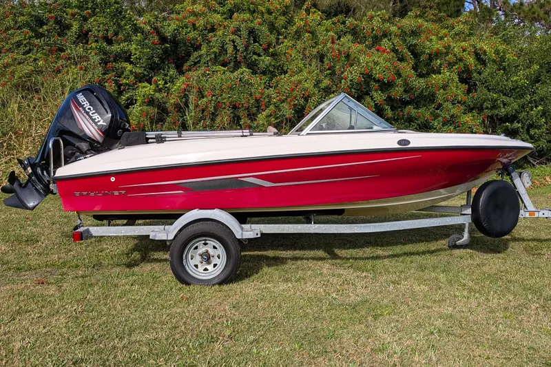 Slide: The Image of 2016 Bayliner 160 Bowrider boat on trailer, red and white design, with Mercury outboard motor. - 2