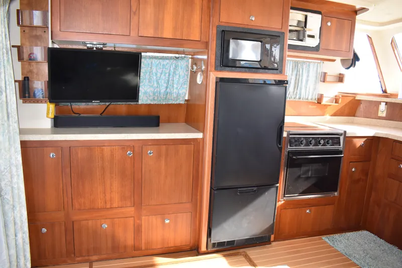Slide: The Image of 2001 Mainship 390 yacht interior with kitchen, featuring wood cabinetry, appliances, and a TV. - 17