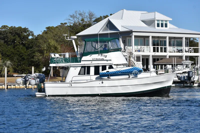 Slide: The Image of 2001 Mainship 390 yacht docked near a waterfront house, with clear blue skies. - 4