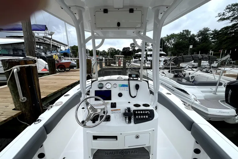 Slide: The Image of 2024 NauticStar 222L Offshore boat dashboard at marina, featuring modern controls and steering wheel. - 6