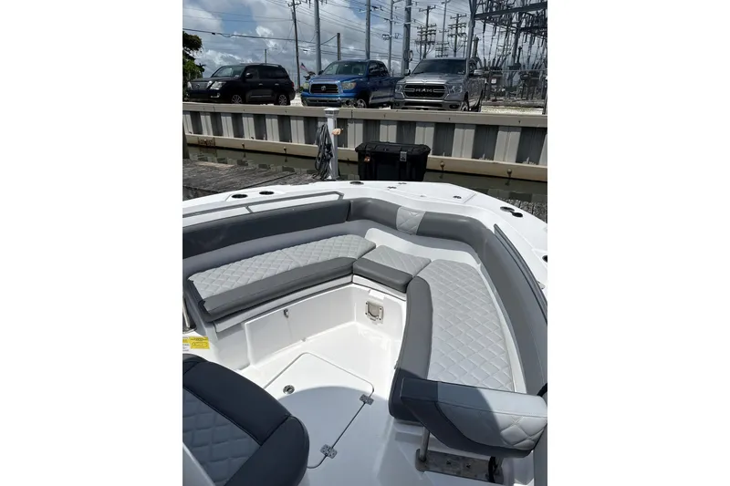 Slide: The Image of 2024 NauticStar 222L Offshore boat with gray seating, docked near parked vehicles. - 7