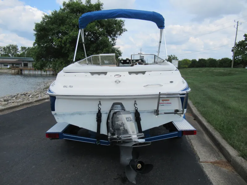 Slide: The Image of 2008 Glastron GXL 185 boat with blue canopy, rear view, parked near a lake. - 2