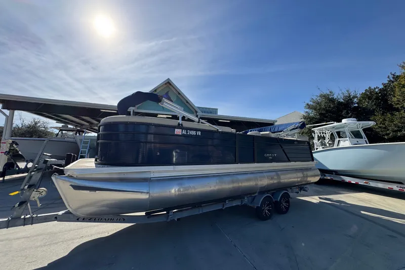 Slide: The Image of 2022 Crest Classic LX 240 SLRC pontoon boat on trailer under sunny sky. - 3