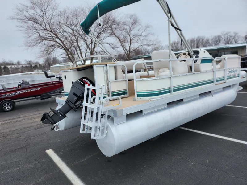 Slide: The Image of Sweetwater 180 pontoon boat, 2000 model, parked on asphalt, with outboard motor and canopy. - 1