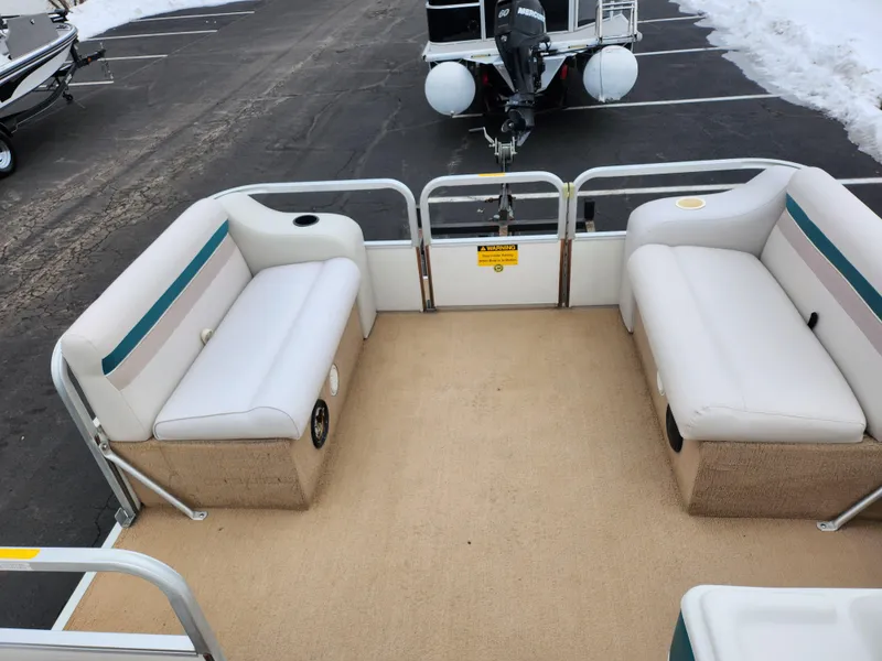 Slide: The Image of Sweetwater 180 pontoon boat, 2000 model, with beige carpet and white seating, parked on asphalt. - 17