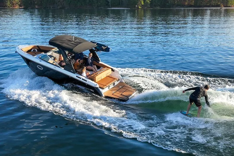 Slide: The Image of Manufacturer Provided Image: 2026 Chaparral GTS 6 boat cruising with a wakeboarder on a sunny lake. - 2