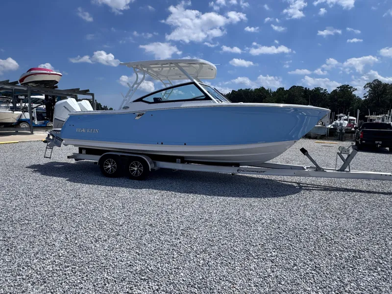 Slide: The Image of 2026 Blackfin 272 DC boat on trailer, parked on gravel under a blue sky. - 7