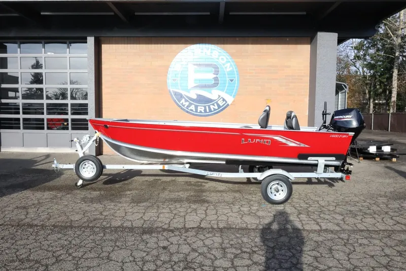The Image of 2026 Lund 1600 Fury Tiller boat on trailer, red exterior, parked outside marine dealership. - 1