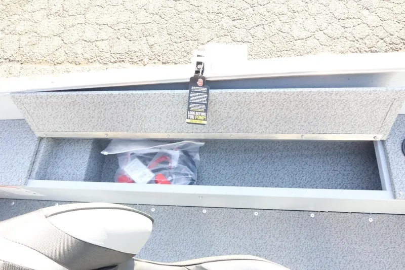 Slide: The Image of 2026 Lund 1600 Fury Tiller boat storage compartment with safety tag and accessories. - 18