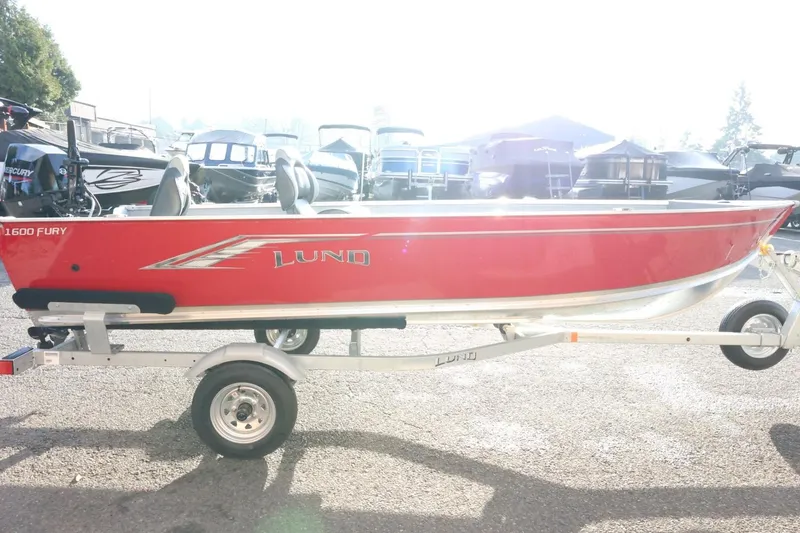 Slide: The Image of Red 2026 Lund 1600 Fury Tiller boat on trailer, parked outdoors. - 6