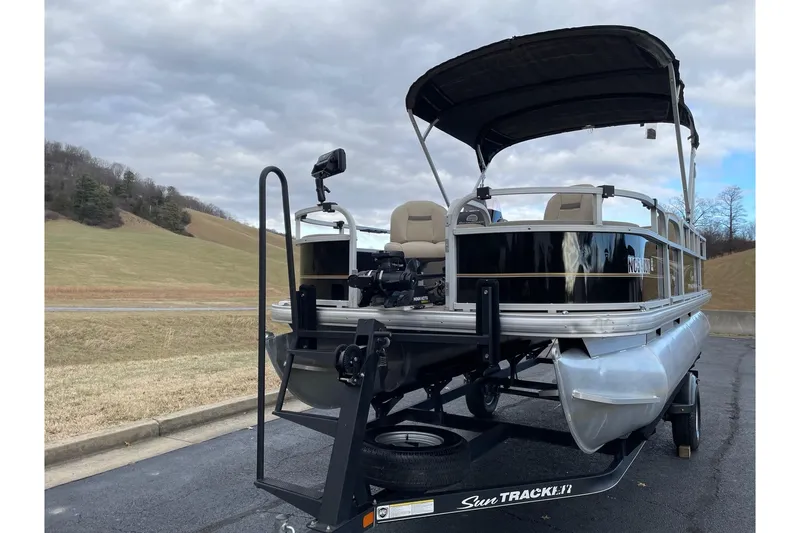 Slide: The Image of 2020 Sun Tracker Bass Buggy 18 DLX pontoon boat on trailer, parked outdoors. - 2