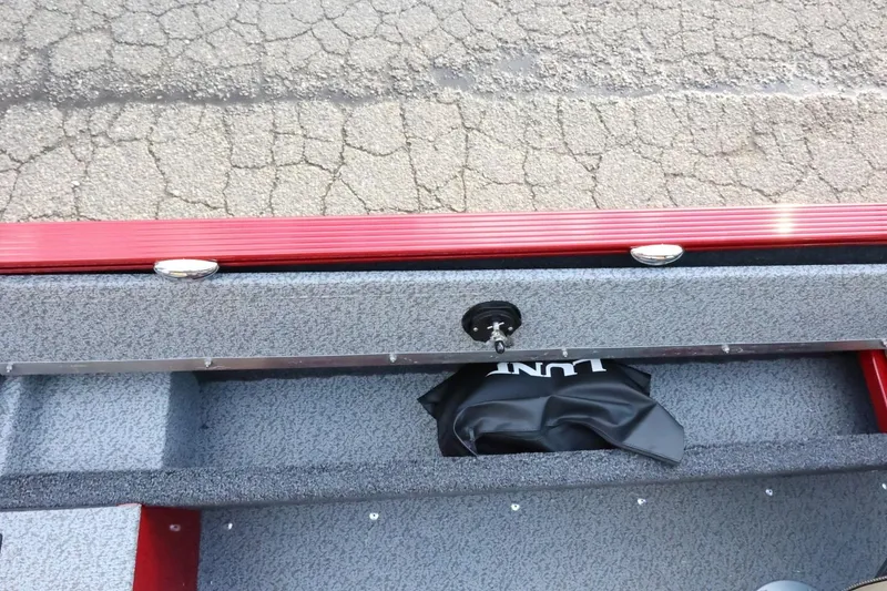 Slide: The Image of 2026 Lund 1650 Angler Sport boat interior with storage compartment and red trim. - 16