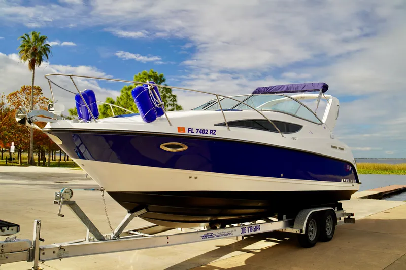 Slide: The Image of 2006 Bayliner 285 boat on trailer, parked near water under a partly cloudy sky. - 7