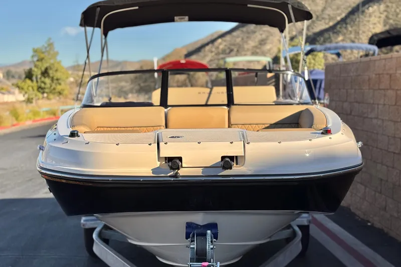 Slide: The Image of 2023 Bayliner DX 2050 boat with beige seating and black canopy, parked on a trailer. - 2