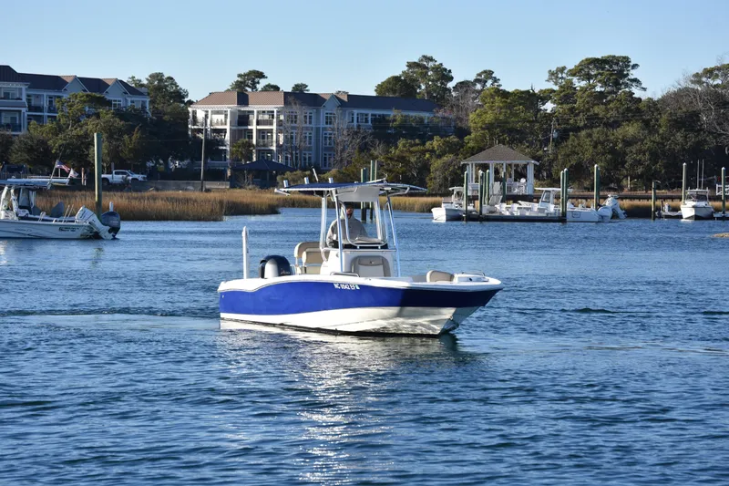 Slide: The Image of 2017 NauticStar 231 Angler boat cruising on a calm waterfront near docks and buildings. - 1