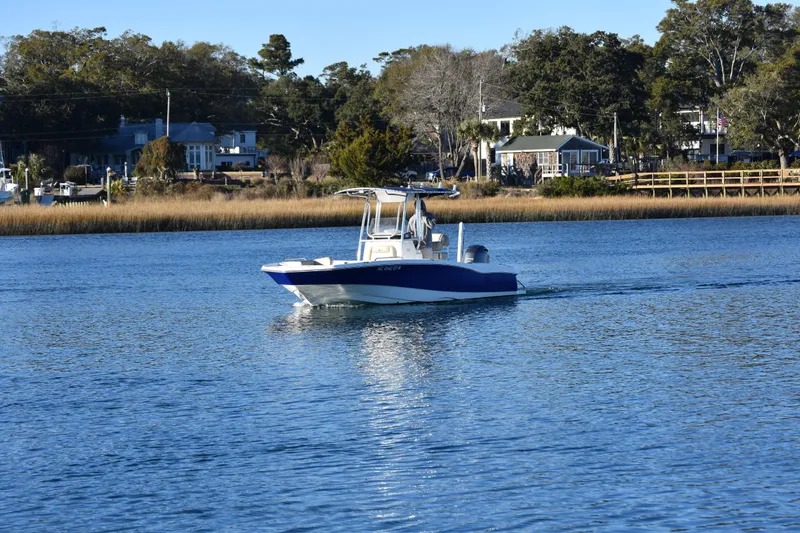 Slide: The Image of 2017 NauticStar 231 Angler boat cruising on a calm lake near a residential shoreline. - 3