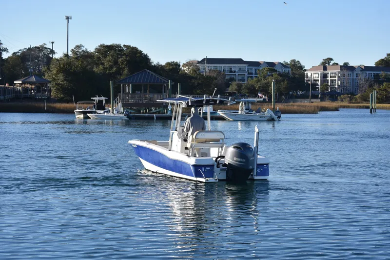 Slide: The Image of 2017 NauticStar 231 Angler boat on calm water near a marina with buildings in the background. - 6