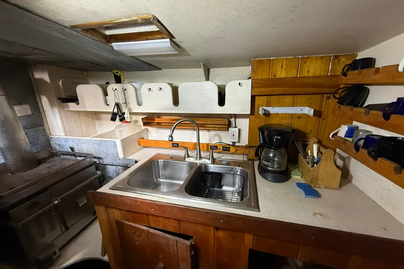 Slide: The Image of Compact kitchen in a 1992 Treworgy 65 Schooner with sink, coffee maker, and wooden shelves. - 16
