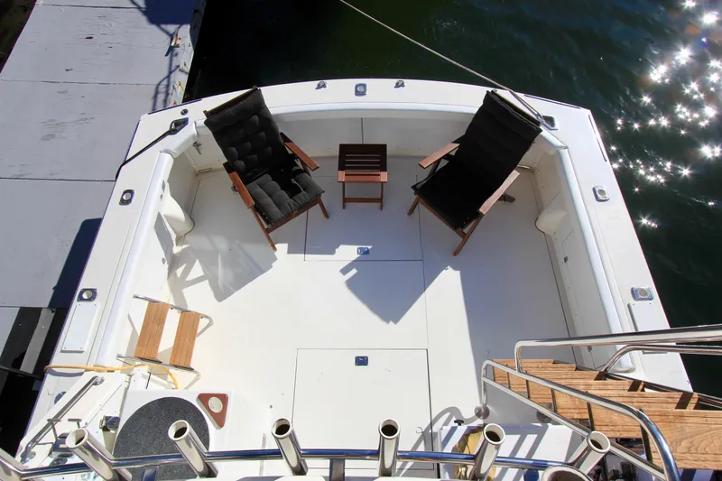 Slide: The Image of Bertram 35 Flybridge 1980 boat deck with chairs and table, docked by sparkling water. - 18