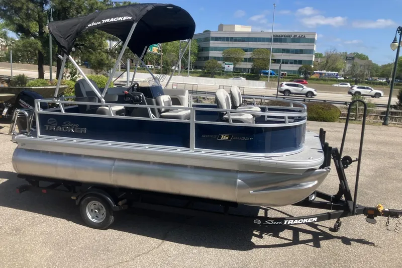 Slide: The Image of 2026 Sun Tracker Bass Buggy 16 XL Select pontoon boat on trailer, parked outdoors. - 4