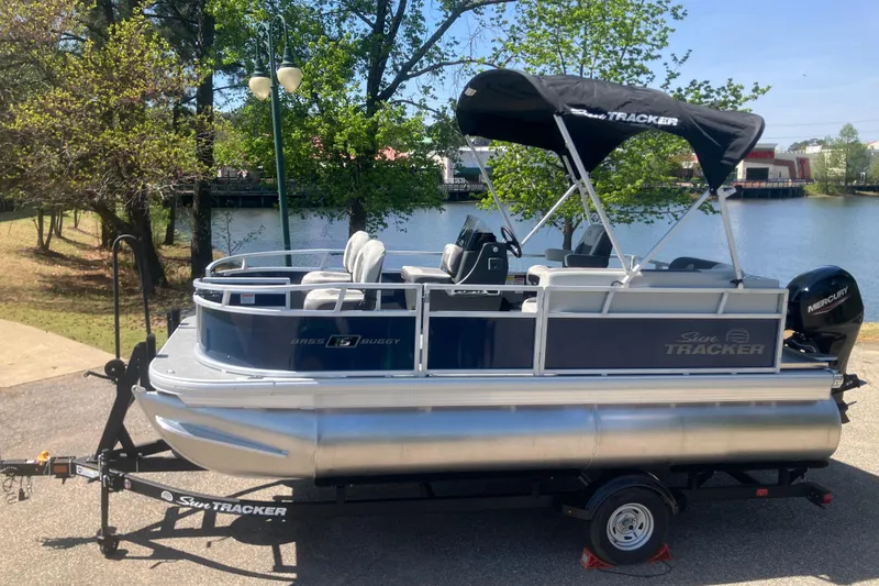 The Image of 2026 Sun Tracker Bass Buggy 16 XL Select pontoon boat on trailer by a lake. - 0