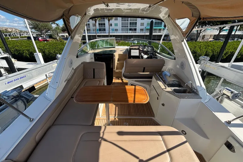 Slide: The Image of 2017 Sea Ray 310 Sundancer interior with seating, table, and helm in marina setting. - 4