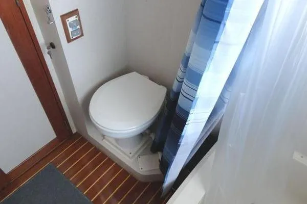 Slide: The Image of 1985 Pearson 43 Trawler bathroom with toilet, striped shower curtain, and wooden floor. - 13