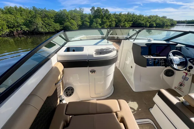 Slide: The Image of 2019 Sea Ray SDX 290 Outboard interior with helm, seating, and lush greenery backdrop. - 10