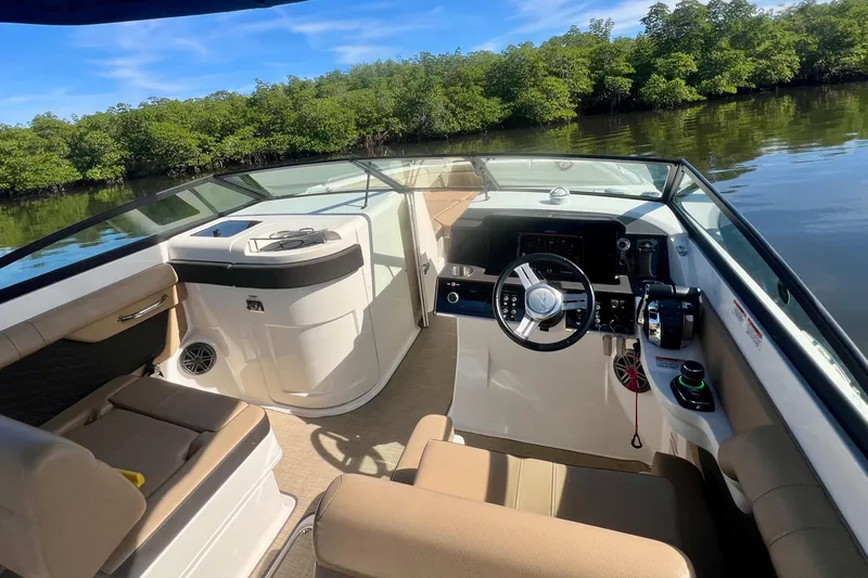 Slide: The Image of 2019 Sea Ray SDX 290 Outboard boat interior with steering wheel and seating, near lush greenery. - 8