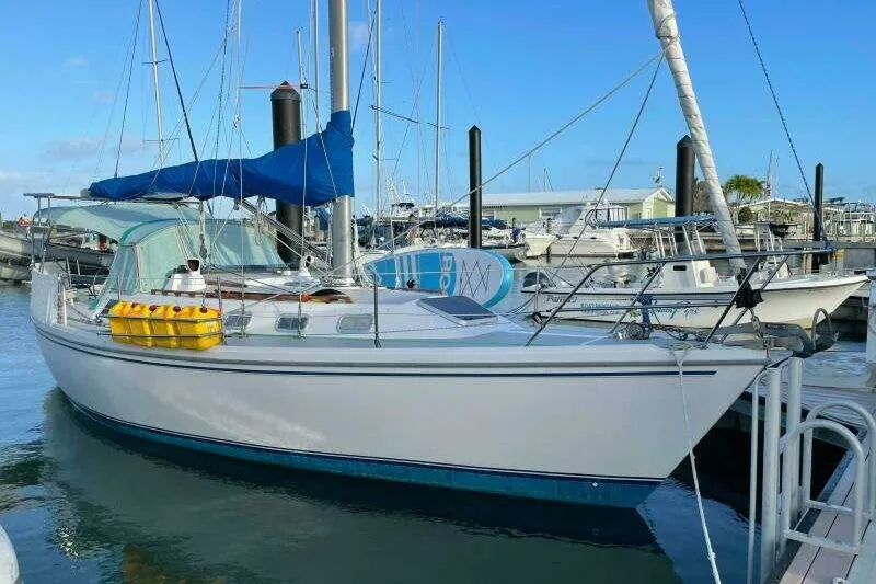 Slide: The Image of 1988 Catalina 34 sailboat docked at marina, featuring blue sail cover and yellow fuel containers. - 2
