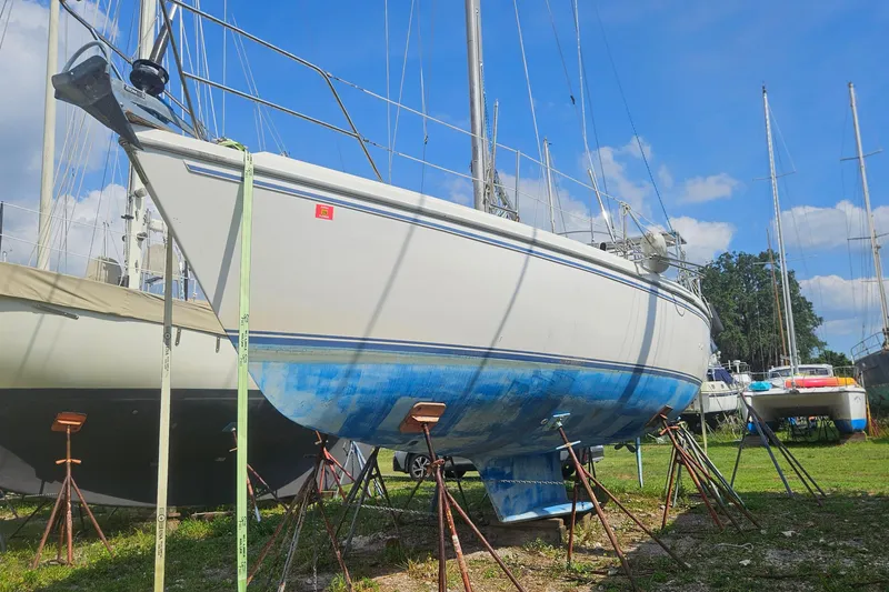 Slide: The Image of 1988 Catalina 34 sailboat on stands, hull painted blue, in a boatyard under clear sky. - 31