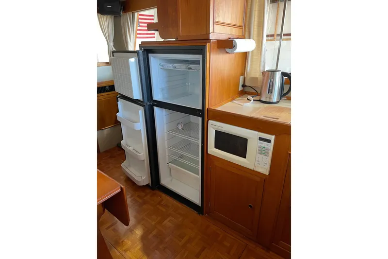 Slide: The Image of 1978 Grand Banks GB36570 interior with fridge, microwave, and kettle in wooden cabinetry. - 11