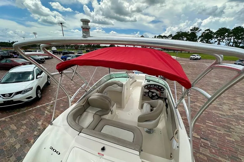 Slide: The Image of 2004 Sea Ray 200 Sundeck with red canopy, parked on brick pavement under cloudy sky. - 16
