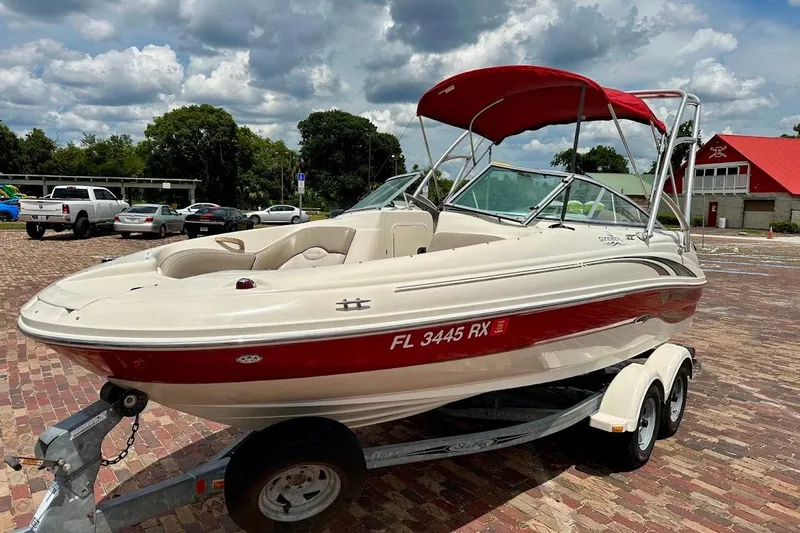 Slide: The Image of 2004 Sea Ray 200 Sundeck boat on trailer with red canopy, parked on brick pavement. - 26