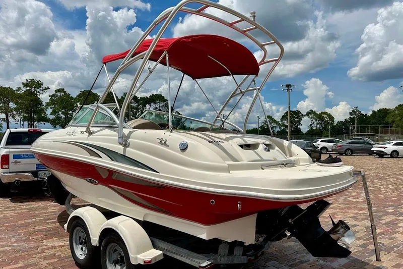 Slide: The Image of 2004 Sea Ray 200 Sundeck boat with red canopy on a trailer, parked outdoors. - 27