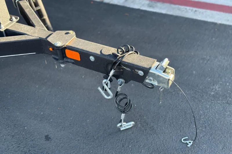 Slide: The Image of Trailer hitch of 2024 Tahoe T21 on asphalt, featuring safety chains and coupler. - 24