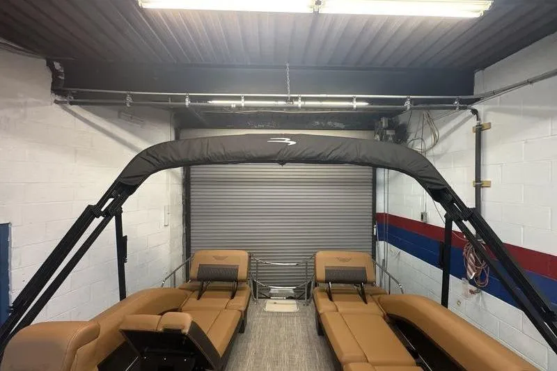 Slide: The Image of 2026 Bennington 24 MSL pontoon boat in a garage with tan seating and black canopy. - 8