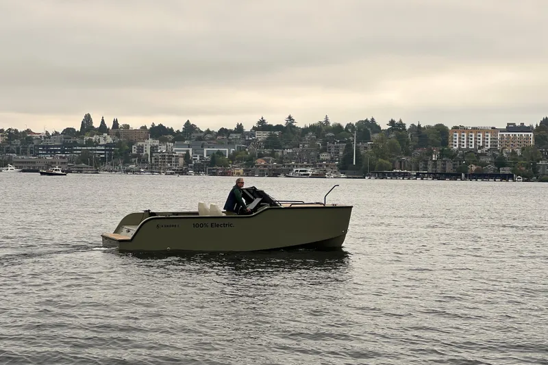 Slide: The Image of 2024 X Shore 1 electric boat cruising on a calm lake with cityscape background. - 1