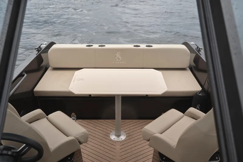 Slide: The Image of 2024 X Shore 1 boat interior with beige seating and table on water. - 9