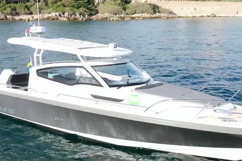 Slide: The Image of 2023 Nimbus Weekender 9 boat cruising near rocky shoreline with lush greenery. - 1