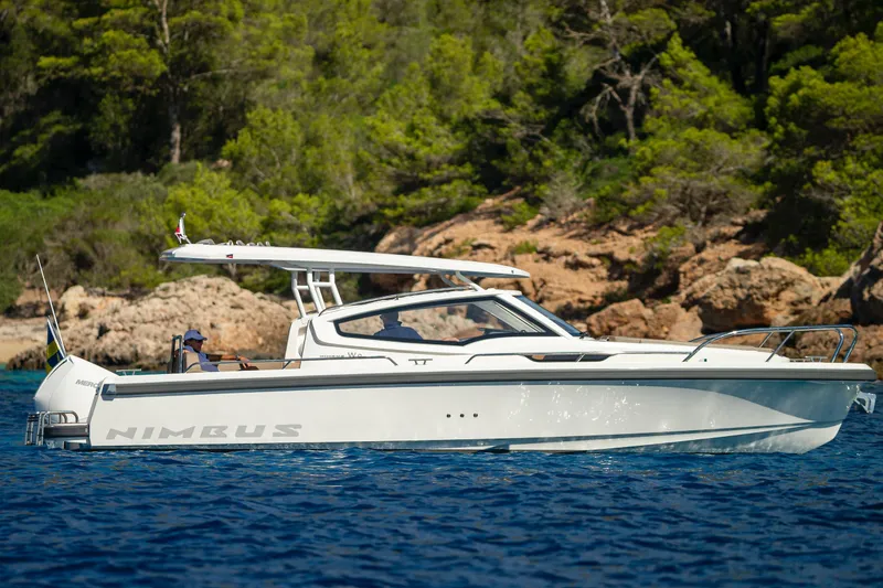 Slide: The Image of 2023 Nimbus Weekender 9 boat cruising near rocky shoreline with lush greenery. - 2