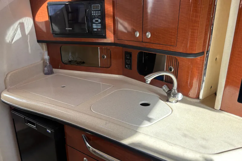 Slide: The Image of 2005 Sea Ray 300 Sundancer kitchen with sink, microwave, and wooden cabinetry. - 8
