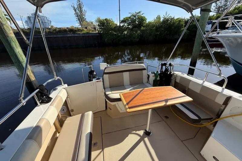 Slide: The Image of 2015 Cutwater 28 boat interior with seating and wooden table, docked by a calm river. - 6