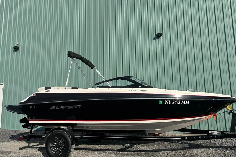The Image of 2016 Larson LX 205S IO boat on trailer, parked by a green metal wall. - 1