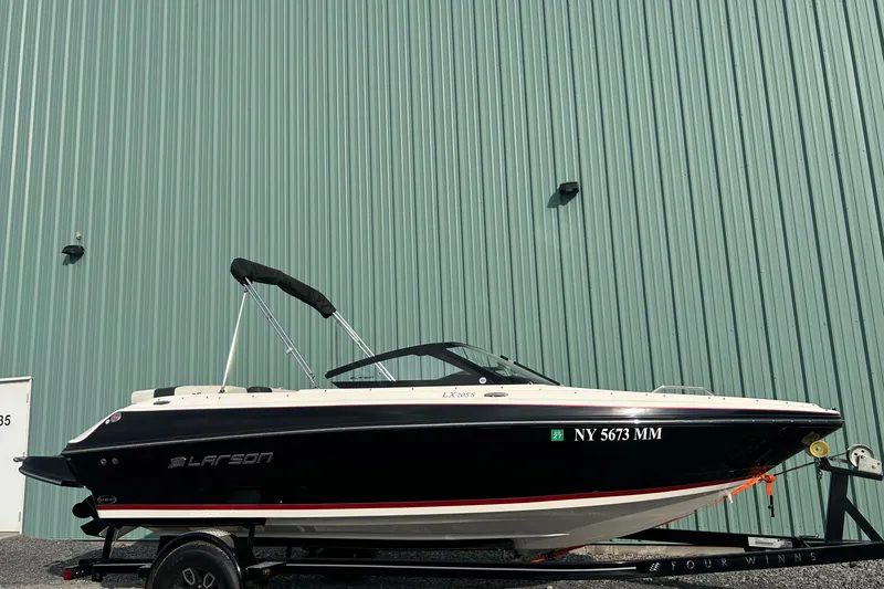 Slide: The Image of 2016 Larson LX 205S IO boat on trailer, parked by a green metal wall. - 3