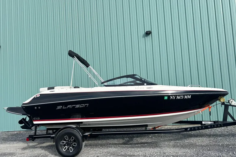 Slide: The Image of 2016 Larson LX 205S IO boat on trailer, parked by a teal building. - 4