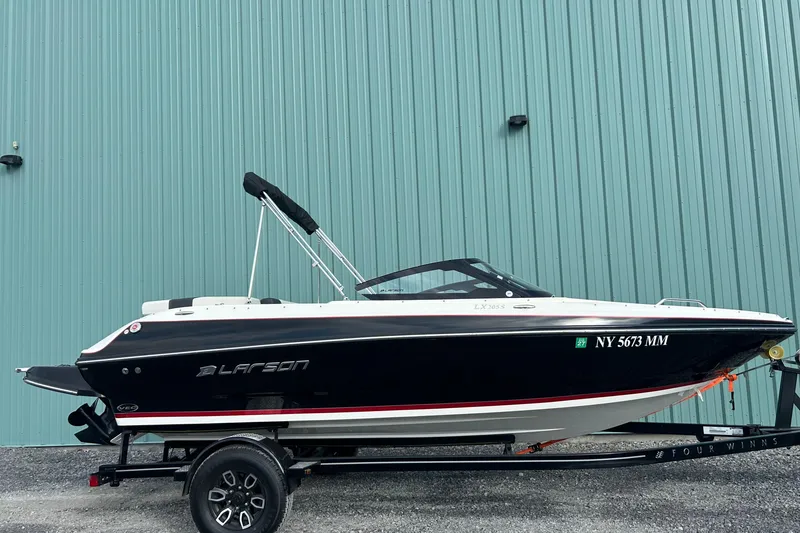 Slide: The Image of 2016 Larson LX 205S IO boat on trailer, parked against a teal wall. - 5