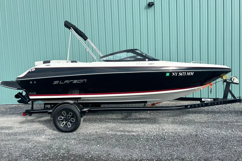 Slide: The Image of 2016 Larson LX 205S IO boat on trailer, parked by a teal wall. - 6